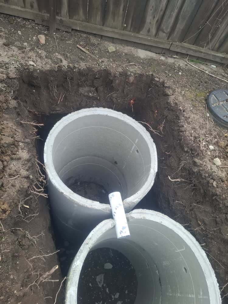 Două tuburi de beton coborâte în groapă și legate între ele, pentru o fosă din două camere.
